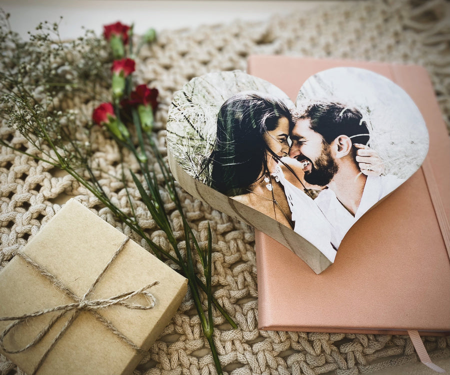 Heart-shaped wooden photo block with couple photo, surrounded by dried flowers and a gift box